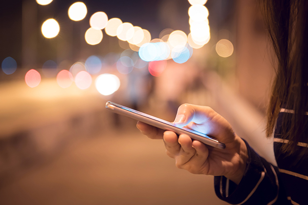 Skru ned for lysstyrken på telefonen når det er mørkt Kvinde står med telefon på station om aftenen