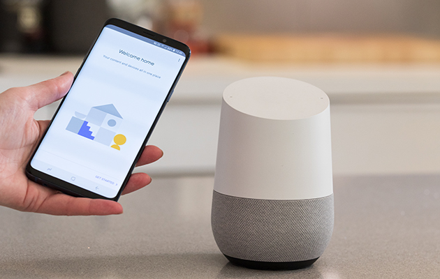 Gør stemmestyring til din måde at tænde og slukke for lyset Billede af en hånd, der holder en smartphone ved siden af en Google Home højttaler
