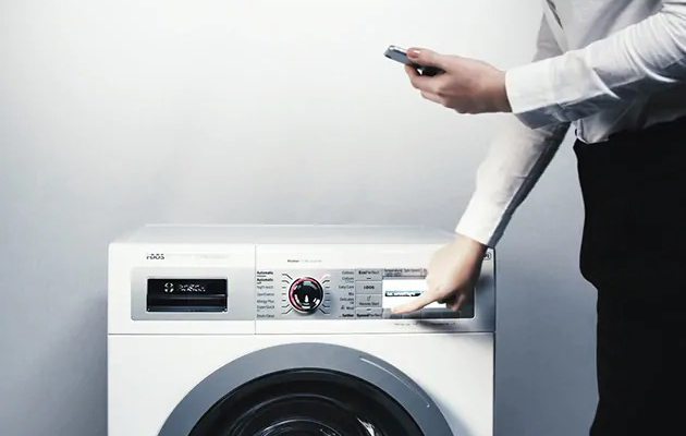 Find det perfekte vaskeprogram i din Home Connect app En mand står med en smartphone i den ene hånd og trykker på en vaskemaskine med den anden