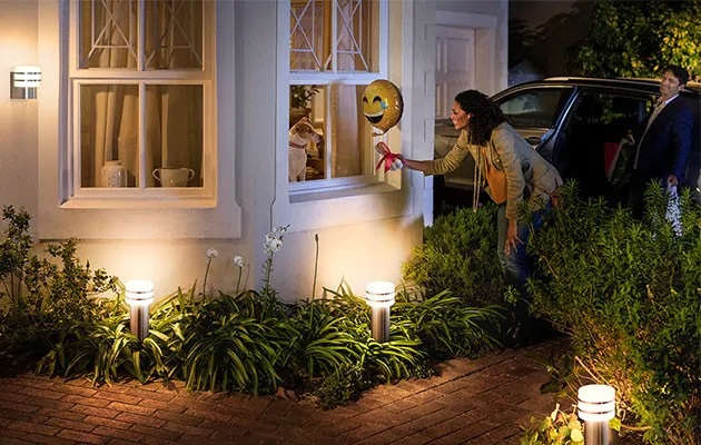 Find inspiration til et bedre smart home En kvinde står udenfor et hus med havebelysning omkring sig. Hun holder en ballon foran et vindue med en hund i.