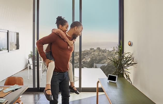 Google nest hub passer naturligt ind overalt i hjemmet Barn på ryggen sin far, begge ser på Google nest hub