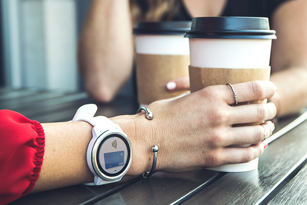 ’kontaktløse betalinger En hånd holder en kaffekop og har et smartwatch om håndleddet.