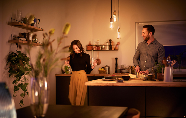 Philips LED Vintage skaber en hyggelig stemning derhjemme Philips LED Vintage hænger i et køkken, hvor en mand og en kvinde laver mad