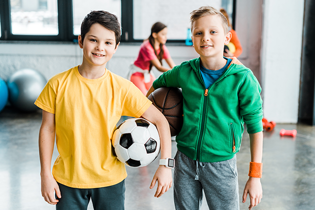 Vælg det rigtige sportsur til dit barn To drenge i gymnastiksal med bolde. Den ene dreng har et sportsur på.