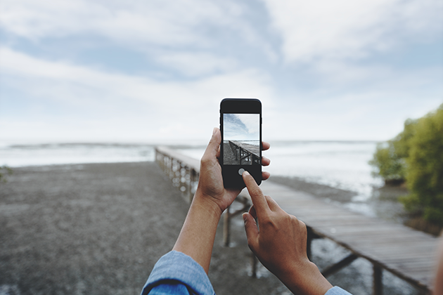 Få tips til at tage bedre billeder med din telefon Person tager billede af strand og badebro med sin mobiltelefon
