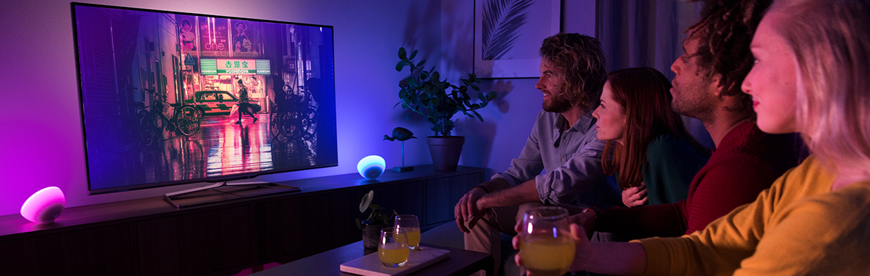 Underholdning Philips Hue smart belysning ved siden af to kvinder og en mand, der ser TV