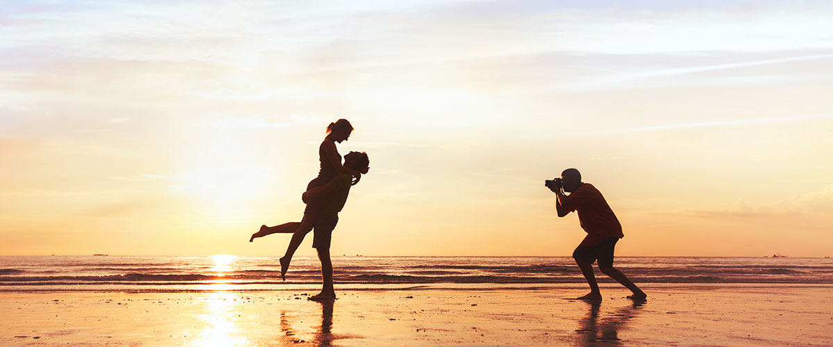 Månedens fotodeal Strand ved solnedgang med silhuetten af en fotograf som fotograferer et dansende par