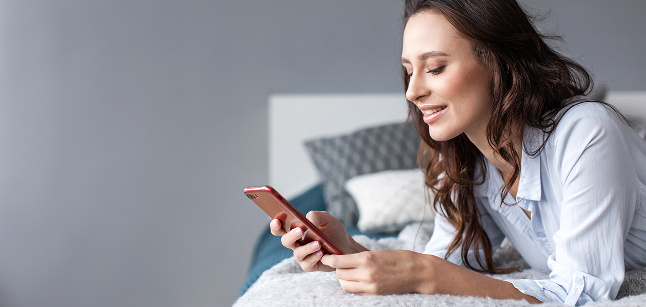 Mindre stress med vores tjenester til mobil Kvinde ligger på seng med en telefon