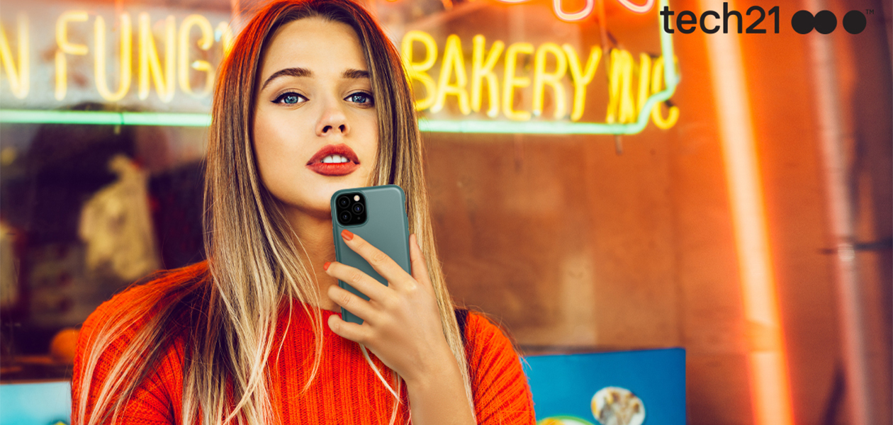 Tech21 beskyttelse Kvinde står foran bageri med iPhone med Tech21 cover i hånden