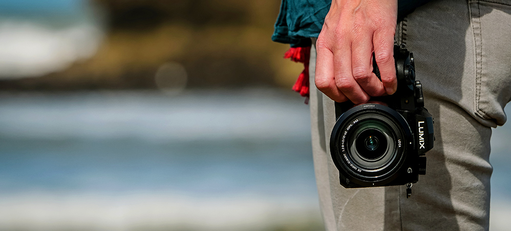 Panasonic LUMIX G90 En hånd holder et sort G90-kamera