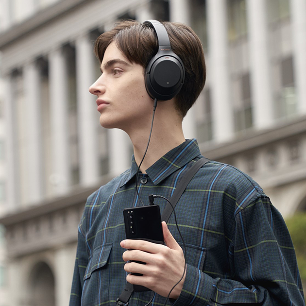 Den ultimative lydkvalitet – med ledning eller trådløst. Du får desuden afbalanceret stereolyd med højtalerne i telefonen Mand med Sony hovedtelefoner på og Sony Xperia 1 II I hånden