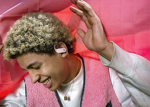 Powerbeats øretelefoner i candyfloss farve En smilende mand med hænderne i luften har candyfloss farvet øretelefoner på