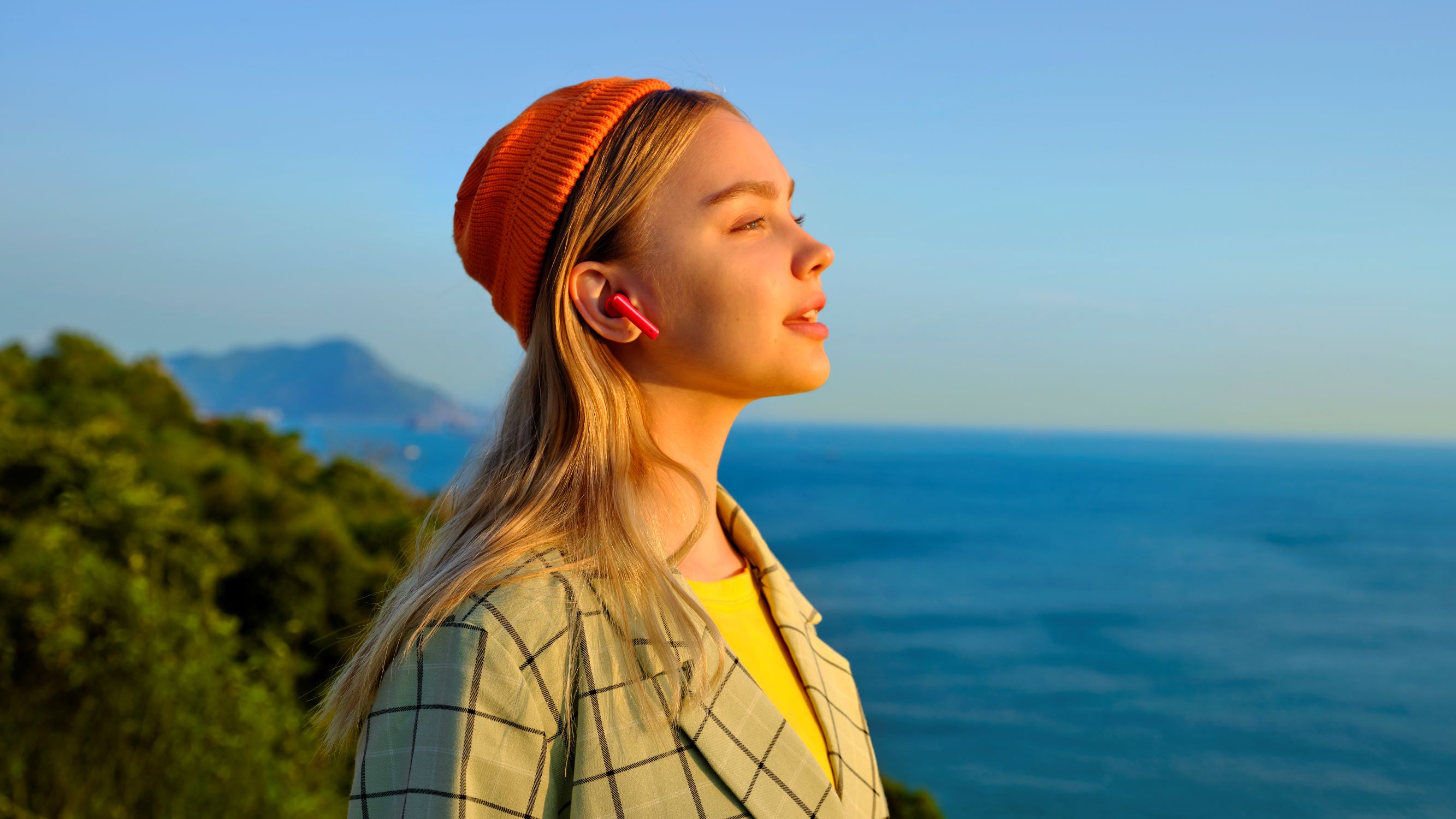 Huawei Freebuds 4i reducerer lyden af vind Kvinde med Huawei Freebuds 4i ser ud over havet