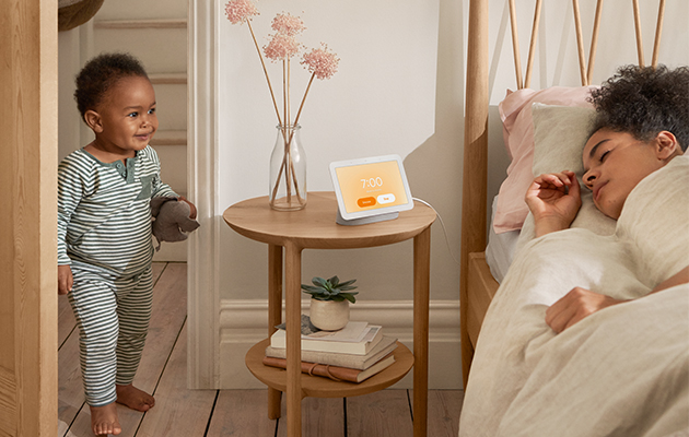 Med Nest Hub på dit natbord kan du nemmere falde i søvn og vågne blidt op En dreng kommer ind på et rum, hvor en kvinde sover ved siden af Google Nest Hub på sit natbord