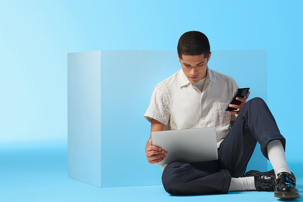 Windows 11 lader dig maksimere kreativiteten Mand sidder på gulvet med en Windows 11-computer og en mobiltelefon