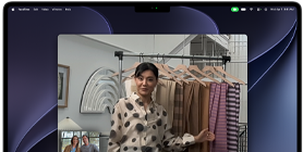 Et videoopkald på en MacBook Pro, hvor en kvinde viser stofprøver til to personer på opkaldet. Centreringsfunktionen holder hende i midten af billedet, når hun går rundt