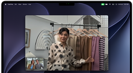 Et videoopkald på en MacBook Pro, hvor en kvinde viser stofprøver til to personer på opkaldet. Centreringsfunktionen holder hende i midten af billedet, når hun går rundt