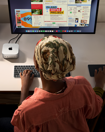 En person sidder ved et skrivebord og skriver med en Mac mini, Studio Display tilsluttet, Magic Keyboard, Magic Trackpad og forskellige ting