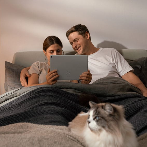 Kvinde og mand i sengen ser Google TV på Google Pixel Tablet og en kat