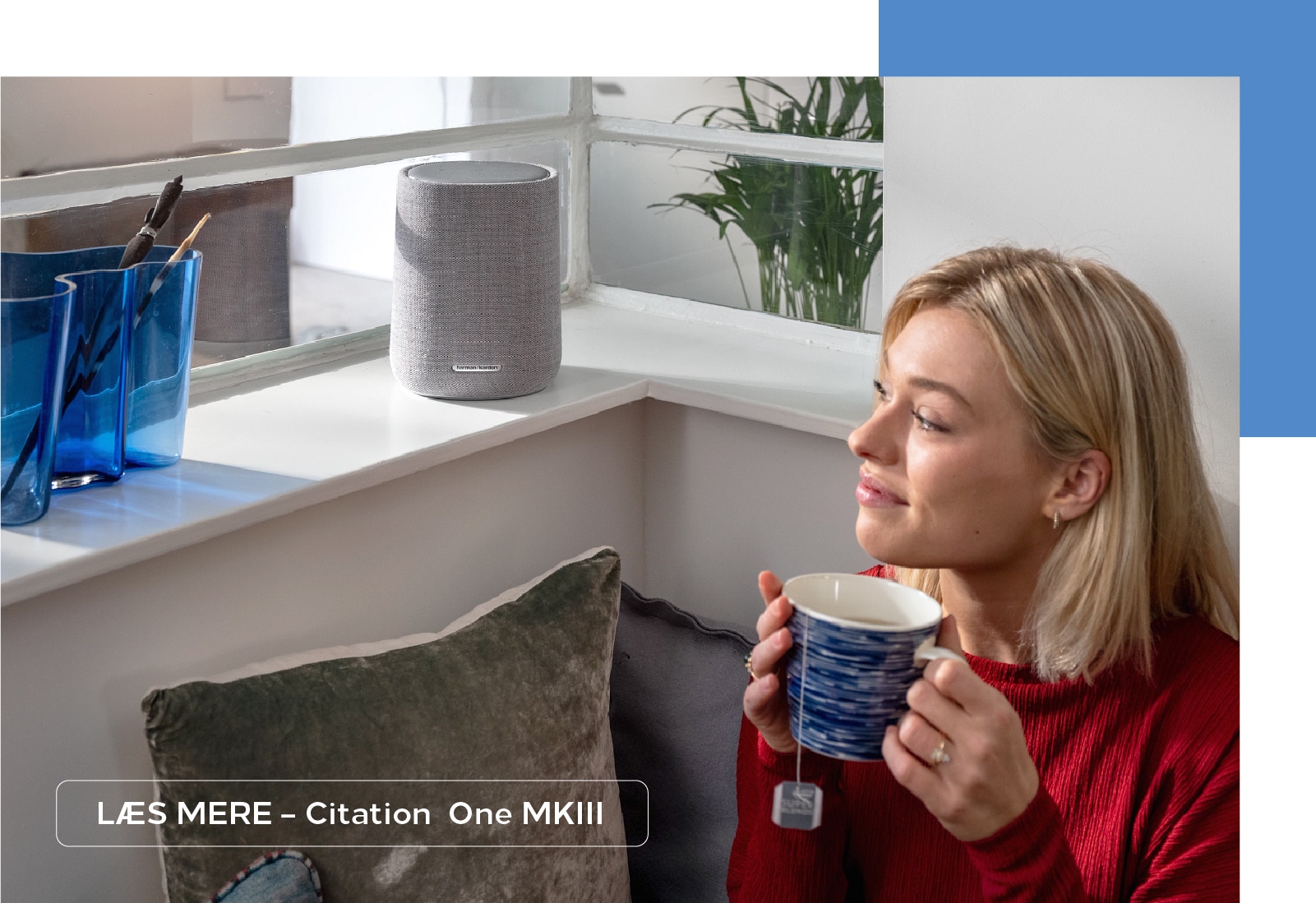 Kvinde der sidder i stue med en kop the i hånden og lytter til en Harman Kardon Citation højttaler