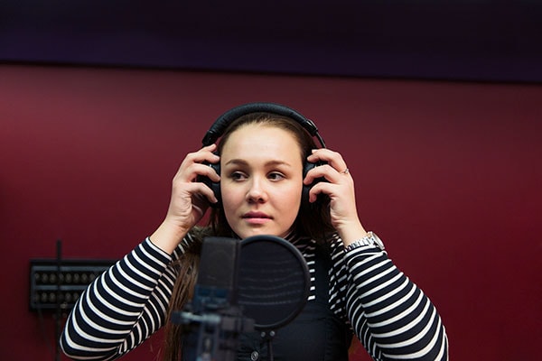 En kvinde med hovedtelefoner på, imens hun indspiller podcast