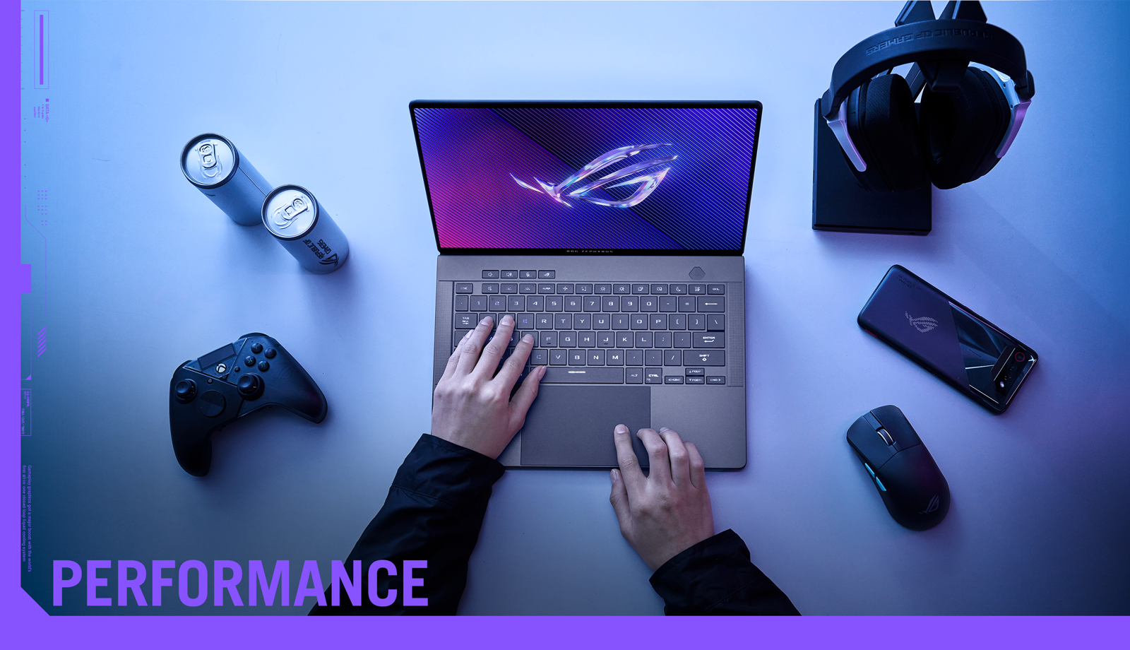 ROG ZEPHYRUS G14 bærbar på et bord med controller, hovedtelefoner, mus og mobiltelefon ved siden af