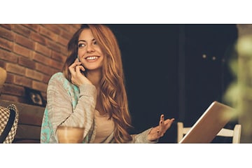 Kvinde der bruger en bærbar mens hun taler i telefon og smiler