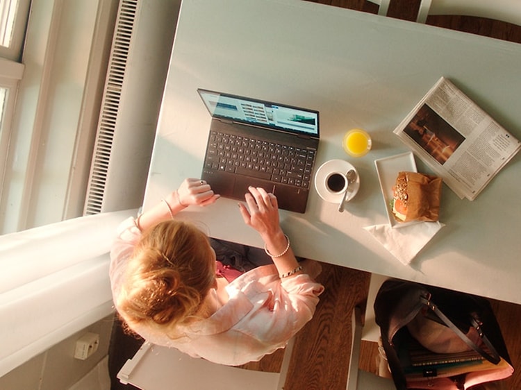 Kvinde der skriver på HP computer mens hun spiser frokost