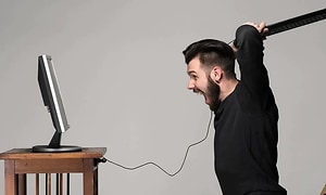 mand bliver sur på sin computer og slår mod skærmen med tastaturet