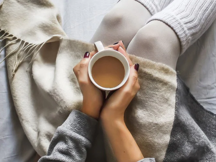 Kvinde med en kop kaffe i en seng