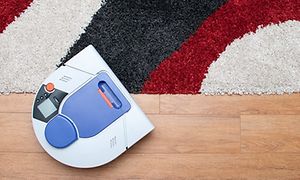 Hvid robotstøvsuger på et trægulv med 3 farvet tæppe ved siden af