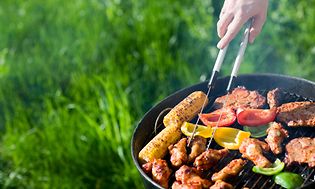 Hånd, der vender kød og grøntsager på en grill