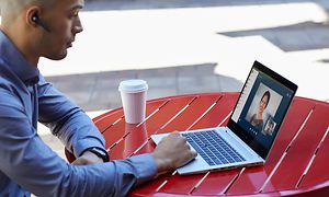 Mand videochatter på laptop udenfor på en cafe