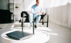 Trådløs router på et bord mens en mand sidder i baggrunden og kigger på sin tablet
