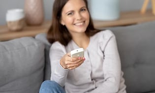 Kvinde der smiler mens hun holder en fjernbetjening til en varmepumpe