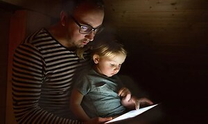 Far og datter bruger en tablet i mørket