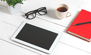 Tablet ved siden af notesbog, briller, krus og plante