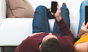 Mand ligger på gulvet og ser på sin smartphone