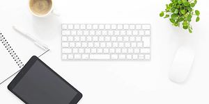 Tablet med et separat tastatur, mus, notesbog, kaffekrus og plante