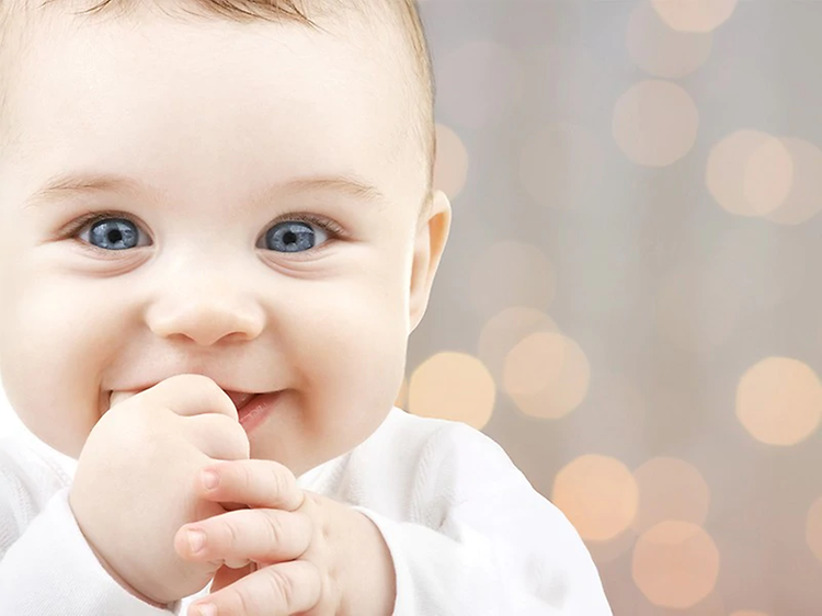 Smilende baby med fingrene i munden