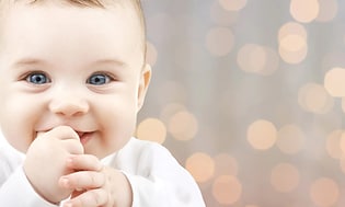 Smilende baby med fingrene i munden