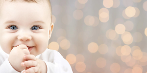 Smilende baby med fingrene i munden