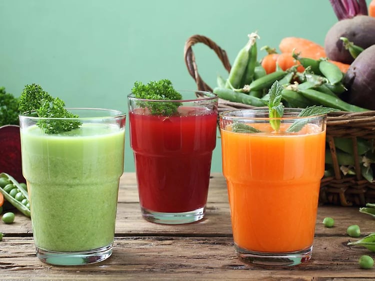 Billede af juicer på et bord med grøntsager i baggrunden