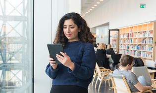 Kvinde, der står i et bibliotek med sin tablet