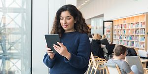 Kvinde, der står i et bibliotek med sin tablet