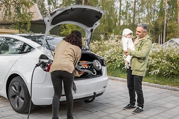 Woman and man with a child, packing a car while it charges