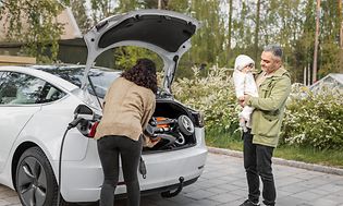 Woman and man with a child, packing a car while it charges