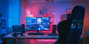 Gamingopsætning med skærm, tastatur og højttalere på et bord, mens en gaming-stoll ses foran det.