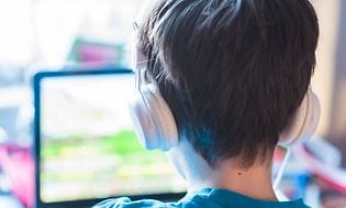 Dreng sidder foran gaming-laptop, mens han har hovedtelefoner på.