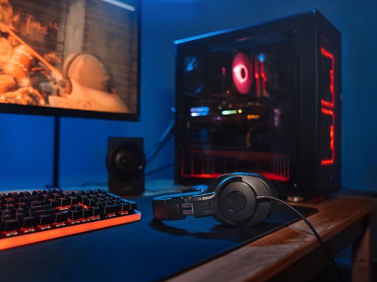 Gaming PC-opsætning med skærm, desktop tower, tastatur og hovedtelefoner, der ligger på bordet